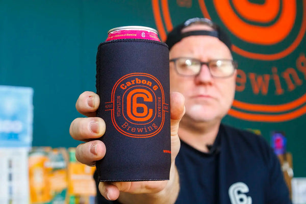 Person holding a Carbon 6 Can Cooler stubby cooler with a can inside, featuring the Carbon 6 Brewing logo.