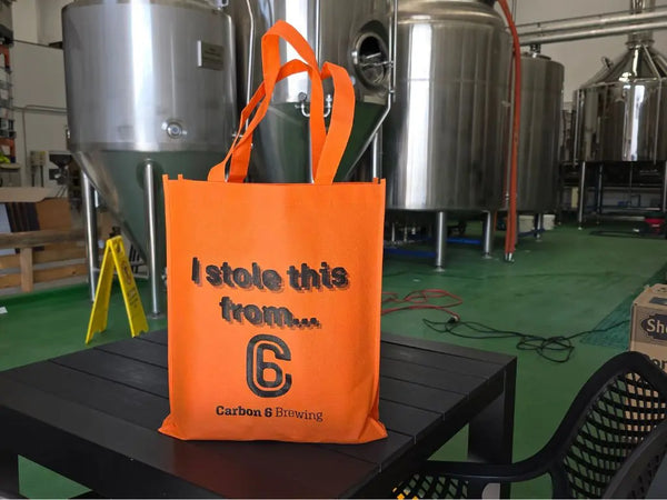 Stolen tote bag featuring bold print 'I stole this from...' in orange, perfect for brewery runs and beach days.