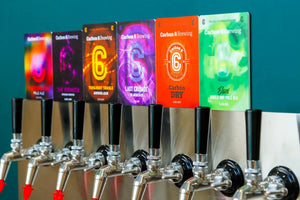 Beers now on tap Carbon 6 Brewing displayed on colorful tap handles at a brewery.