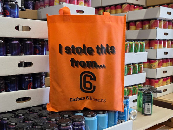 Stolen tote bag in orange with the text 'I stole this from...' displayed, set among beer cans from Carbon 6 Brewing.