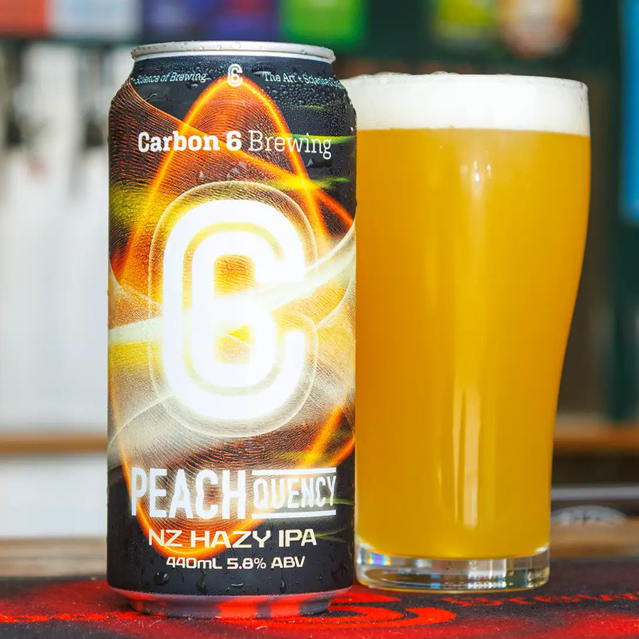 Peachquency Hazy IPA can next to a glass of beer; featuring vibrant colors and branding from Carbon 6 Brewing.
